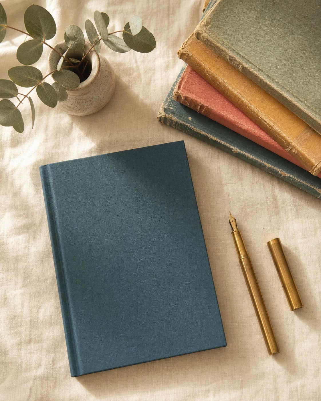 Flat-lay of the guided journal beside a stack of books, eucalyptus, and a brass pen